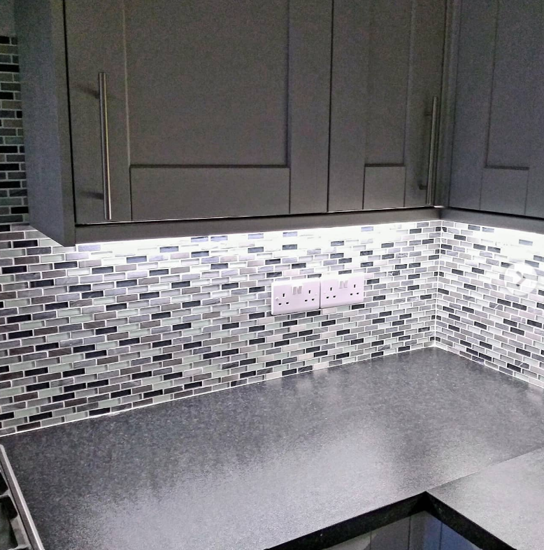 Kitchen worktop lit by under-cabinet LED strips, with double sockets on a mosaic splashback