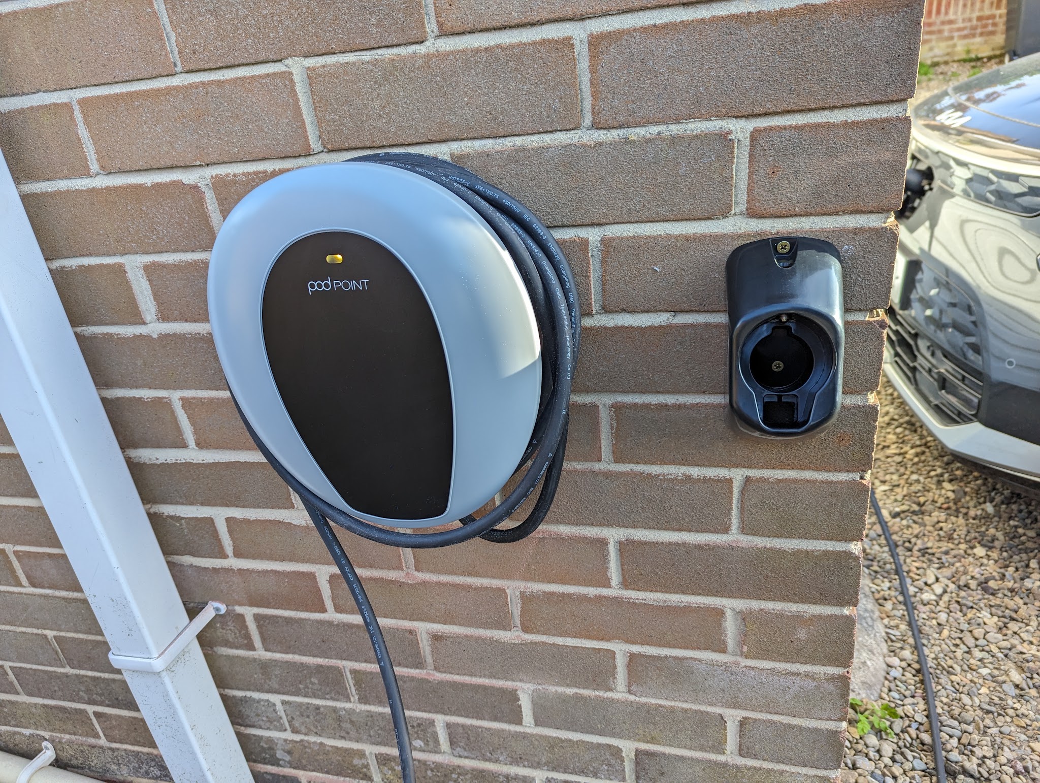 Pod Point electric vehicle charger installed on a brick wall beside a driveway